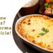 Travessa com arroz de forno cremoso recém-saído do forno, com queijo derretido e gratinado por cima, em uma mesa rústica com colher de servir ao lado.